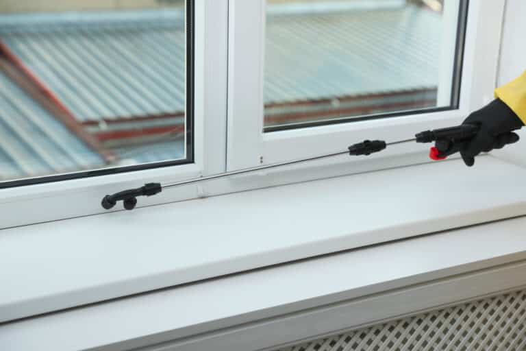 Pest control worker in protective suit spraying insecticide on window sill indoors, closeup